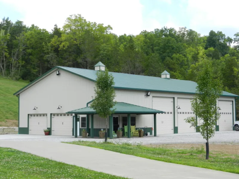 White commercial pole barn with a green metal roof, five overhead doors, and a covered entry porch