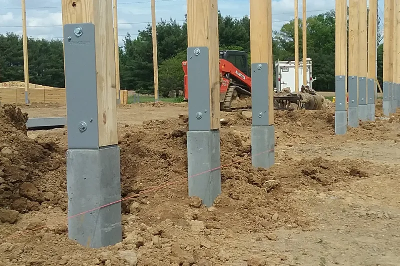 Rows of laminated columns set on poured concrete piers at a pole barn building site