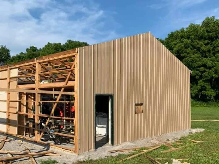Pole barn mid-renovation with new tan steel siding on one wall and the adjacent wall stripped to exposed framing