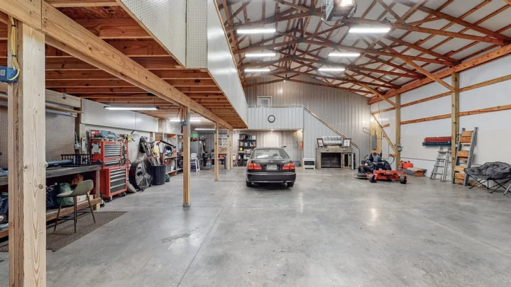 Pole barn shop interior with exposed timber trusses, a mezzanine loft, workbench area, and concrete floor