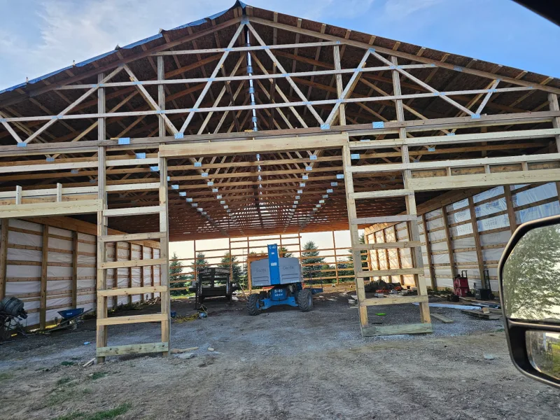 Large post-frame building under construction with exposed roof trusses