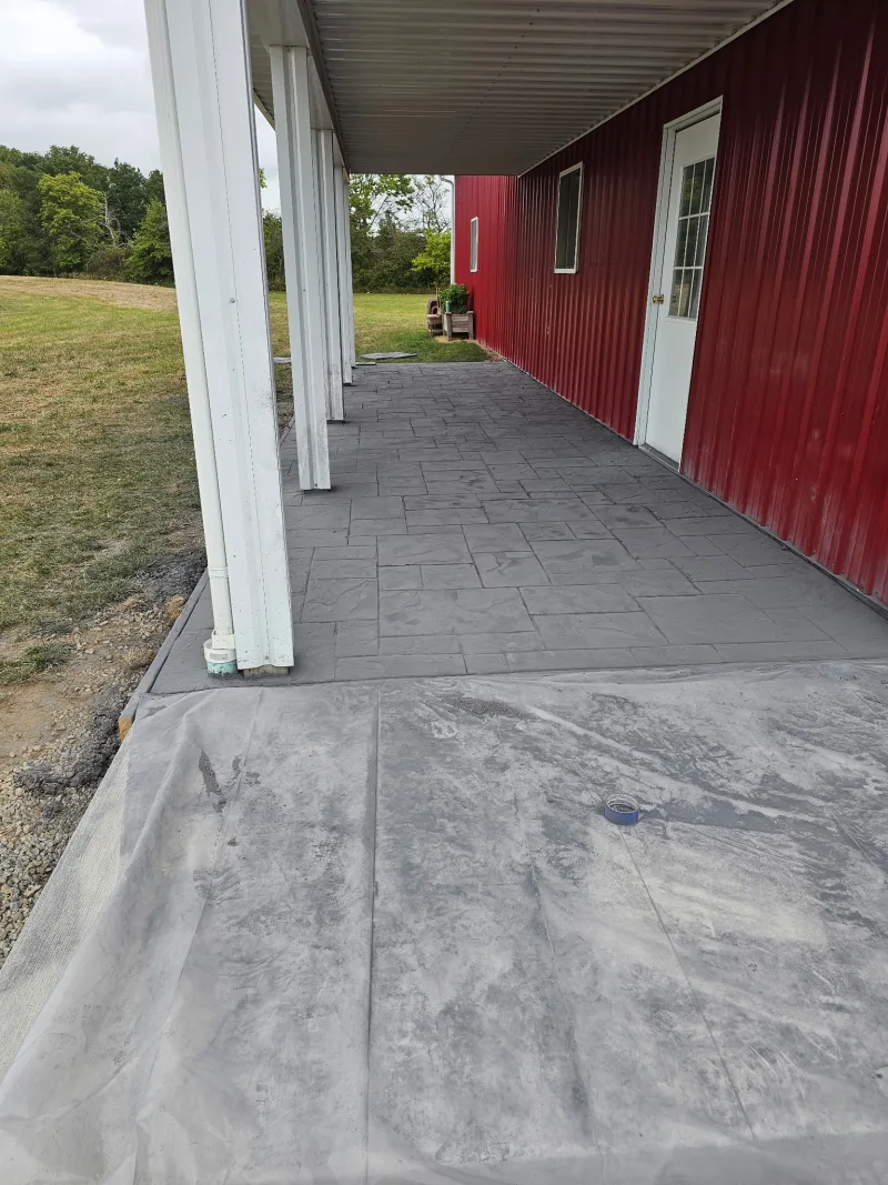 Red pole barn side entrance with stamped-concrete walkway under a lean-to